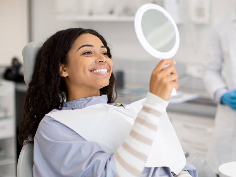 lady holding a mirror smiling in dental chair