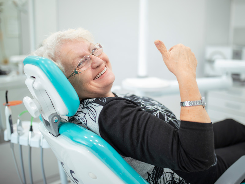 lady smiling in dental chair with thumbs up