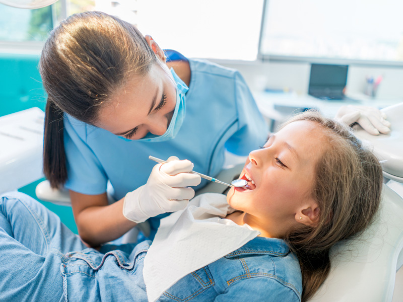 dentist working on kids teeth in dental chair